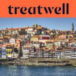 Les quais de la Ribeira à Porto, avec leurs rangées de maisons colorées et de toits en terracotta qui grimpent la colline depuis le Douro, et la tour des Clérigos à l'horizon sous un ciel bleu limpide.