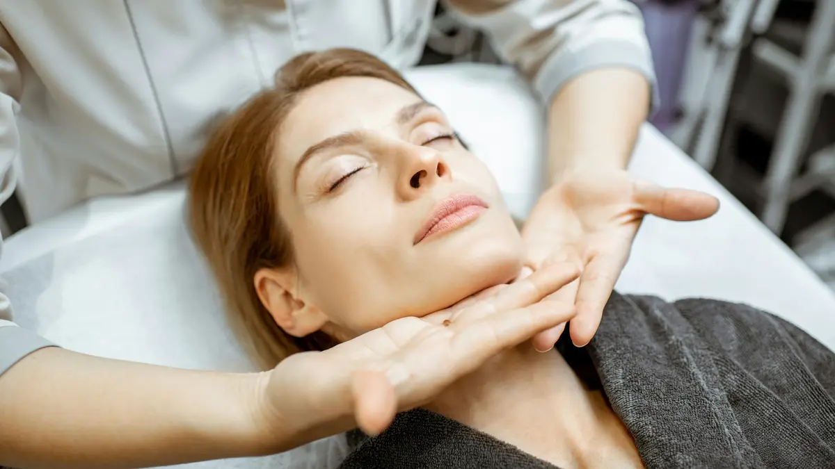 Femme détendue pendant un drainage lymphatique du visage, les mains du praticien glissant délicatement sous sa mâchoire